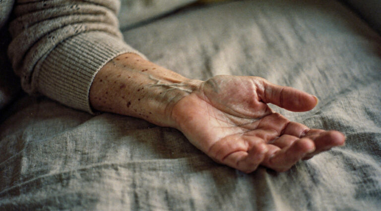 A woman's forearm resting on a bedspread in late evening light, the skin change of menopause.