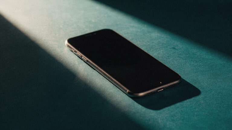 A smartphone lying face-down on a teal kitchen counter in a shaft of hard light, screen dark, the moment after a message goes unsent