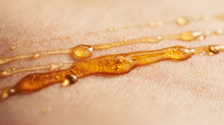 An abstract macro photograph of golden amber oil beading and separating on a pale surface