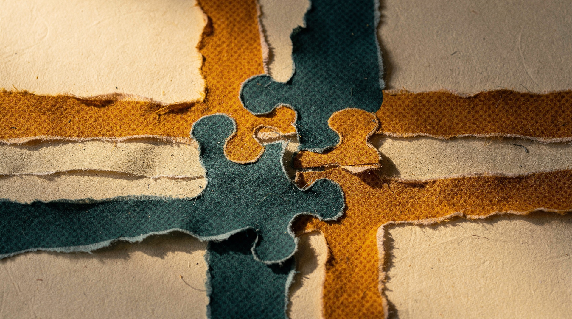 Torn paper collage in ochre and teal on cream, with two jigsaw pieces that do not quite fit together