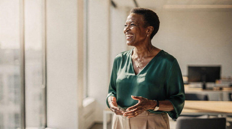 A woman in her fifties in a deep green blouse laughing mid-conversation at a bright office window