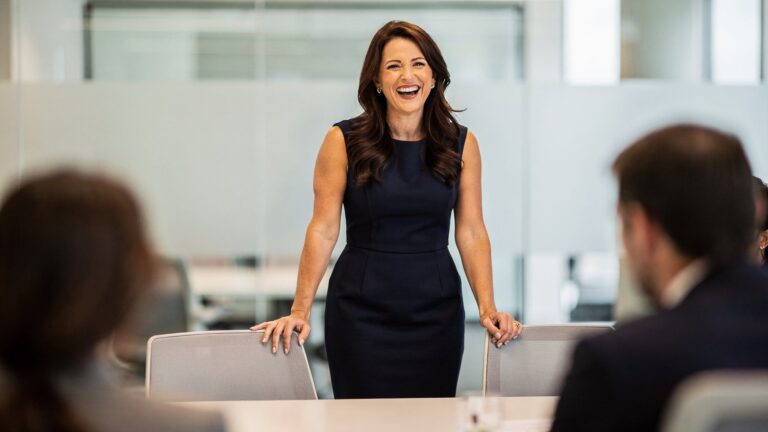 Brunette woman in her mid-forties laughing at the head of a meeting table, relaxed after finding the right hot flash medication