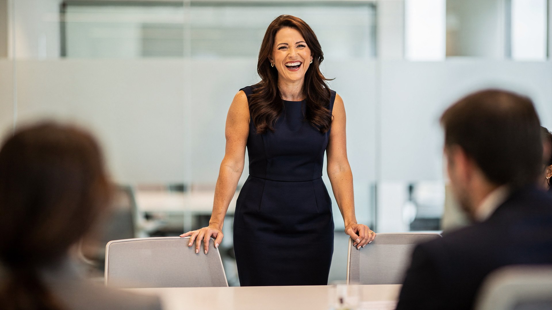 Brunette woman in her mid-forties laughing at the head of a meeting table, relaxed after finding the right hot flash medication